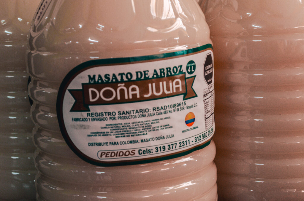 Close-up of a 4-liter bottle of 'Masato de Arroz Doña Julia', traditional Colombian rice milk, with the label detailing health registration, producer information, and contact numbers for orders.