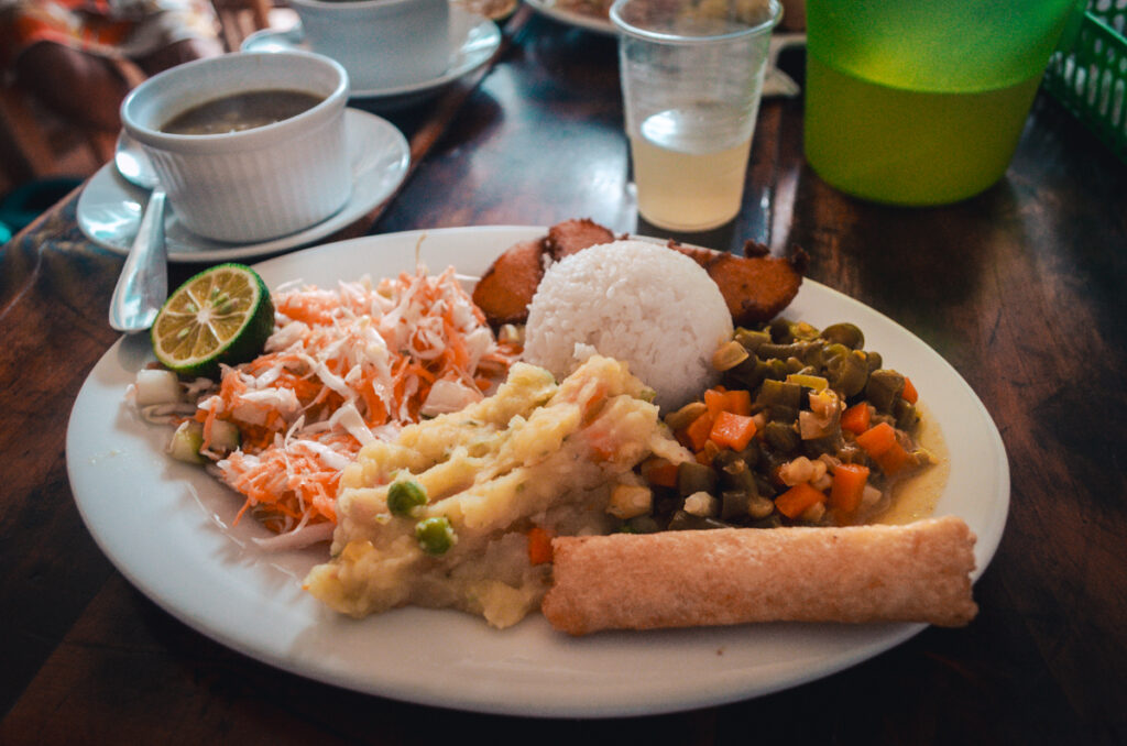 Traditional Colombian almuerzo in Salento,Colombia. This photo shows a plate of rice, potato stew, fried yucca, salad, cooked vegetables and a lentil stew and aguapanela on the side.