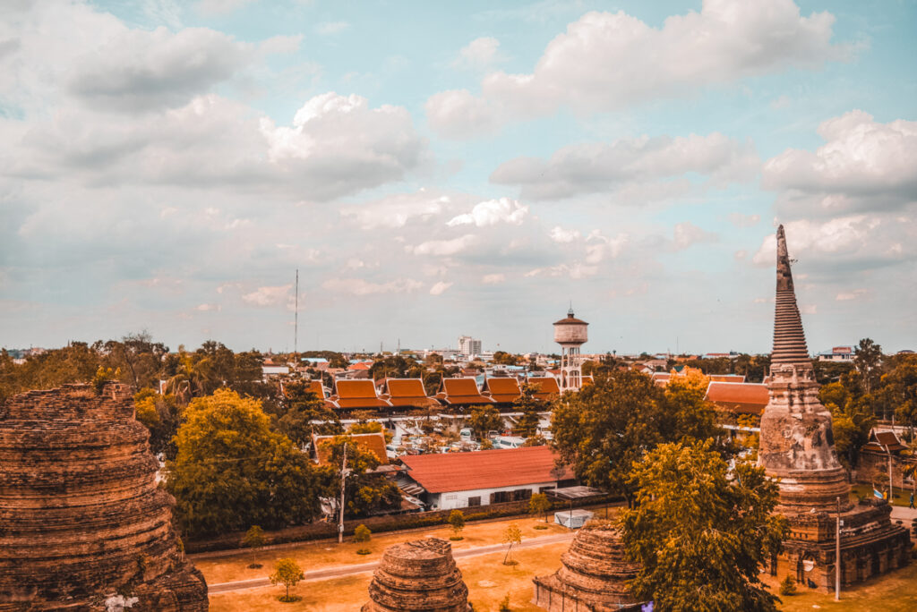 A panoramic view of Ayutthaya's landscape showcases the harmony between the ancient temples and the modern town. Historic structures mingle with contemporary buildings under a vast sky, revealing the city's ability to blend its storied past with the present.