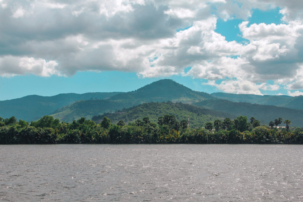 Scenic view of the Bokor Mountain in Kampot, Cambodia, with lush greenery in the foreground and the mountain's peak rising against a cloudy sky.