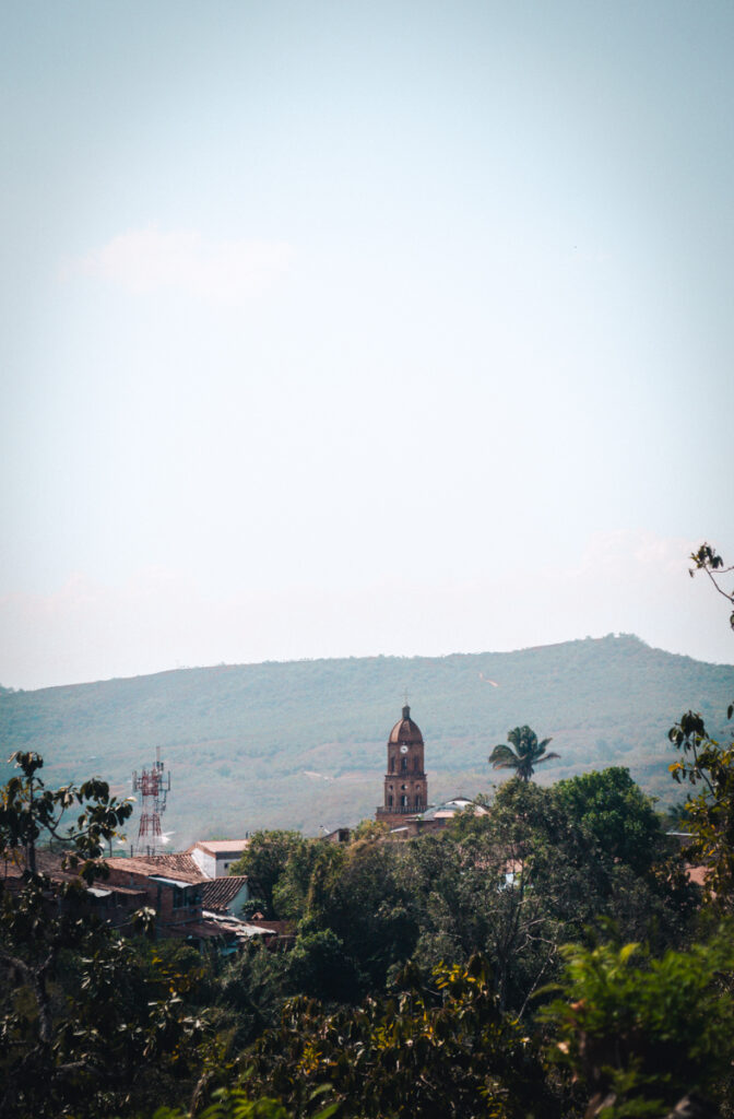 The bell tower of the Church of Curiti stands tall, piercing the sky above the lush greenery and rolling hills of Pescaderito Curiti, Colombia.