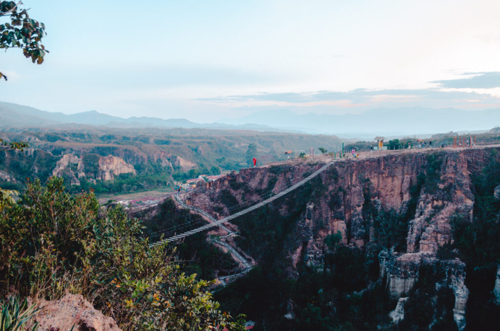 Dusk settles over a dramatic canyon with a suspension bridge connecting the rugged cliffs, while the panoramic view showcases the vast and tranquil landscape surrounding La Playa de Belen, Colombia.