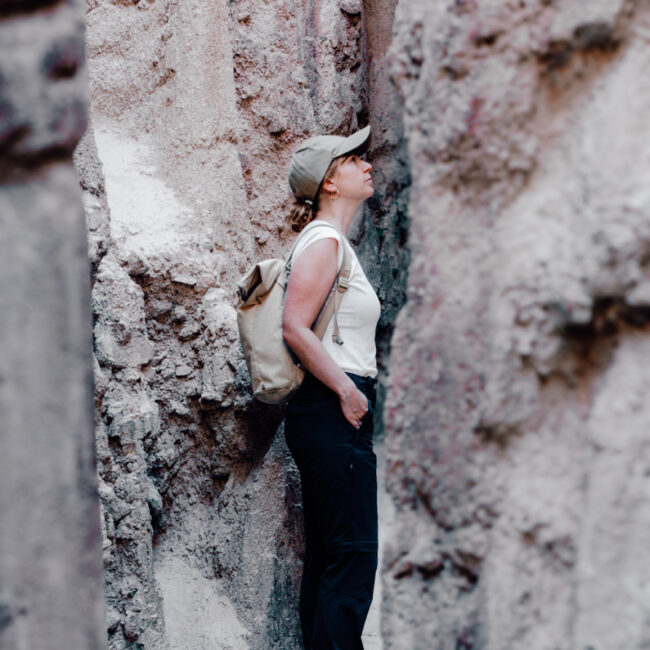 A female hiker looks up in awe at the towering, rugged walls of a narrow passage, emphasizing the grandeur and intricacy of the natural clay formations within Los Estoraques Unique Natural Area.