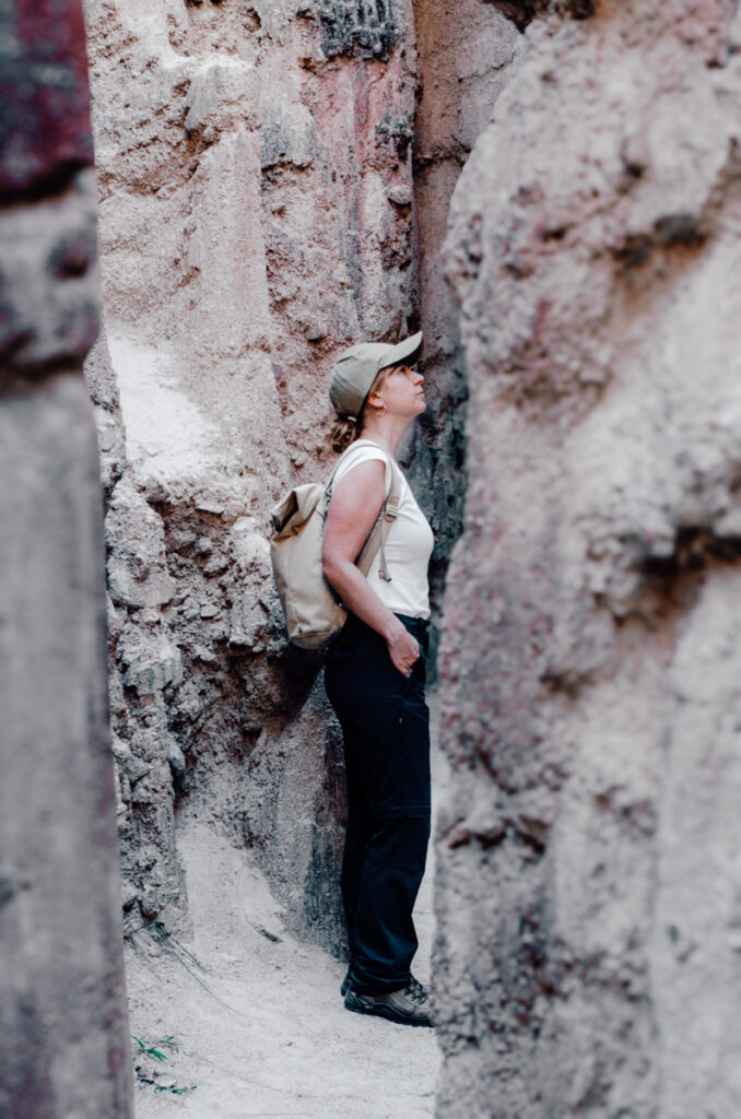 A female hiker looks up in awe at the towering, rugged walls of a narrow passage, emphasizing the grandeur and intricacy of the natural clay formations within Los Estoraques Unique Natural Area.