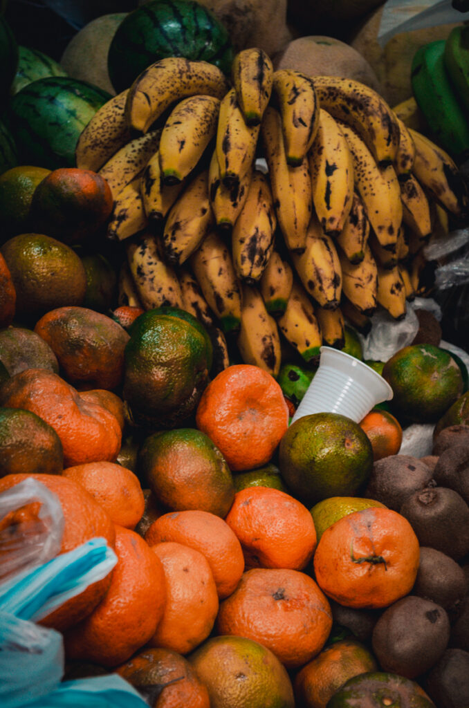 Close-up of ripe bananas above a pile of tangerines and kiwis, showcasing the fresh produce variety available at Paloquemao market in Bogota, Colombia.