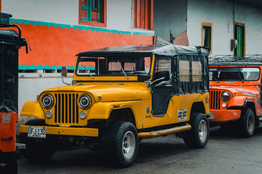 Vintage yellow and orange Willys Jeeps parked in Salento, Colombia, with vibrant, colorfully painted buildings in the background, reflecting the region's traditional transportation and rich cultural heritage.