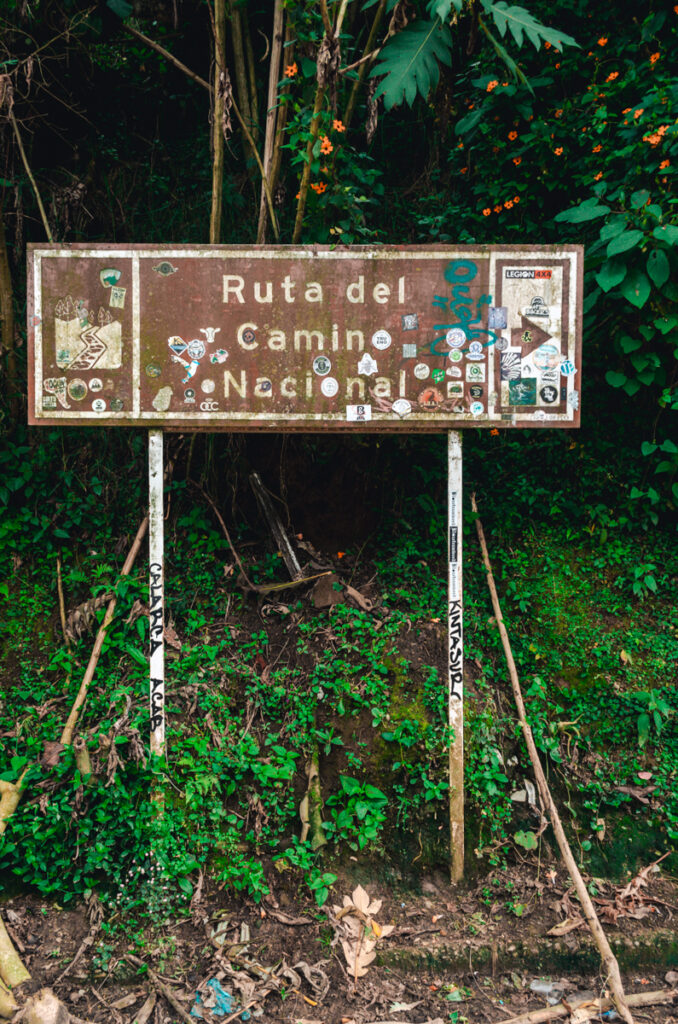 The weathered sign for the Ruta del Camino Nacional in the Zona Cafetero near Salento, Colombia, covered in stickers, stands as a testament to the travelers and hikers that have traversed this path.