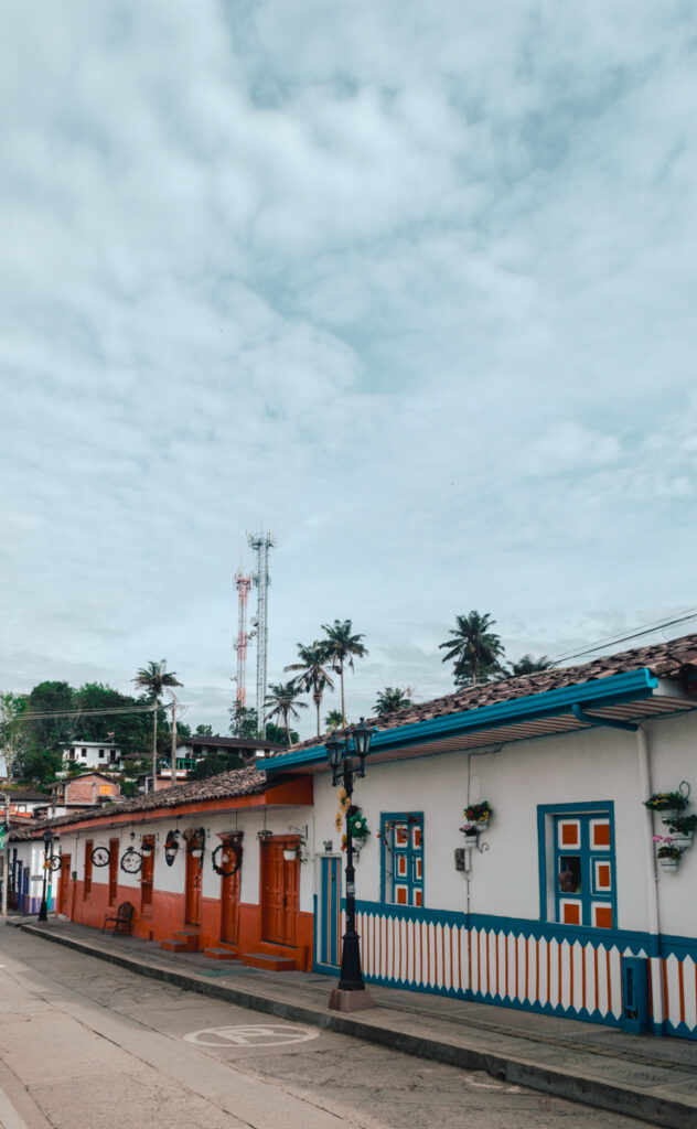 Colorful colonial-style houses line the streets of Salento, Colombia, with a striking orange and blue façade set against a soft, cloud-filled sky, capturing the town's vibrant architectural charm.