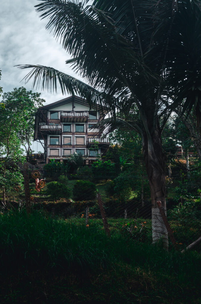 A traditional house or hotel in Salento, Colombia, nestled amid lush greenery and towering palms, its balcony-framed windows offering a glimpse of the area's tranquil, natural beauty.