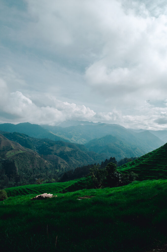 Expansive views of rural fields around Salento, Colombia, with dramatic clouds casting shadows over the vibrant green hills, inviting outdoor enthusiasts to explore the Zona Cafetero’s serene environment.
