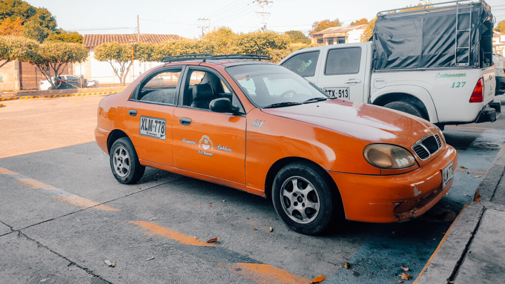 An orange taxicab parked on a sunny street in Colombia, with the license plate "XLM-778" and signage indicating public service for the region, showcasing a glimpse into the local transportation of Aguachica to Ocana.
