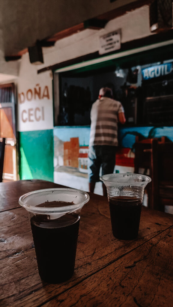 A man standing at a counter of a bar next to the mercado in Barichara. Two hot cups of coffee are standing in front at a table..