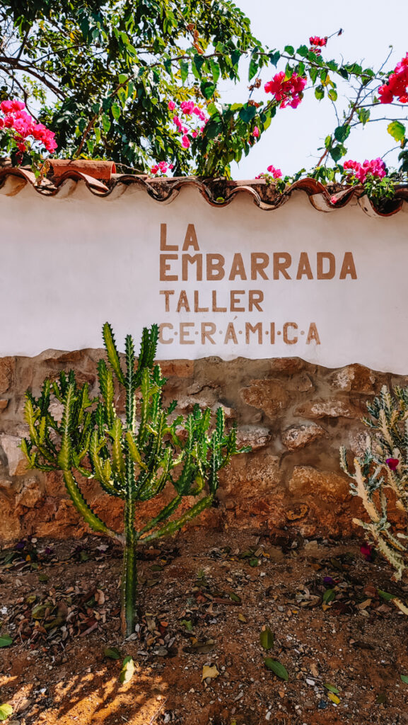 Facade of a ceramic atelier called 'La Embarrada'. The letters are golden on a white background and there's a tropical cactus in front of the wall.