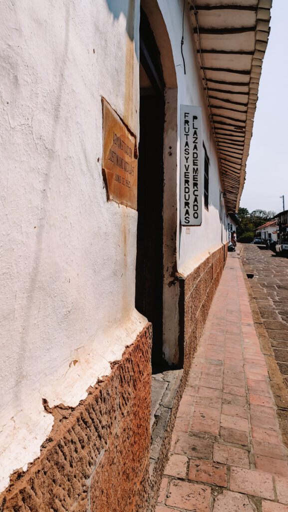 A narrow street with a sign on the wall, indicating the name and direction of the local market in Barichara.