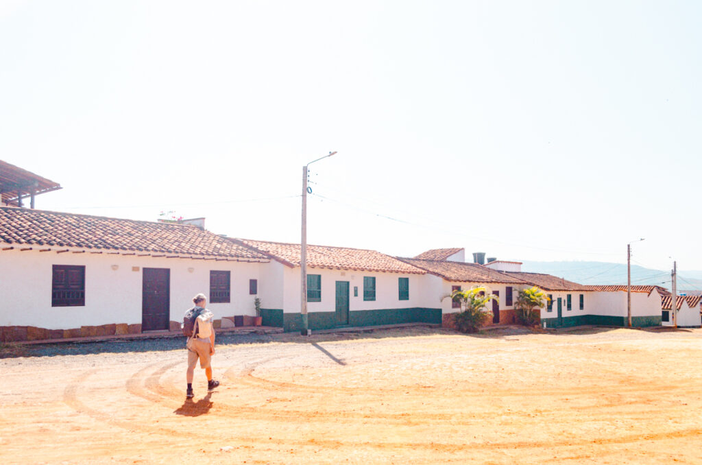 A man strolling along a dirt road in Barichara with traditional houses lining the road.
