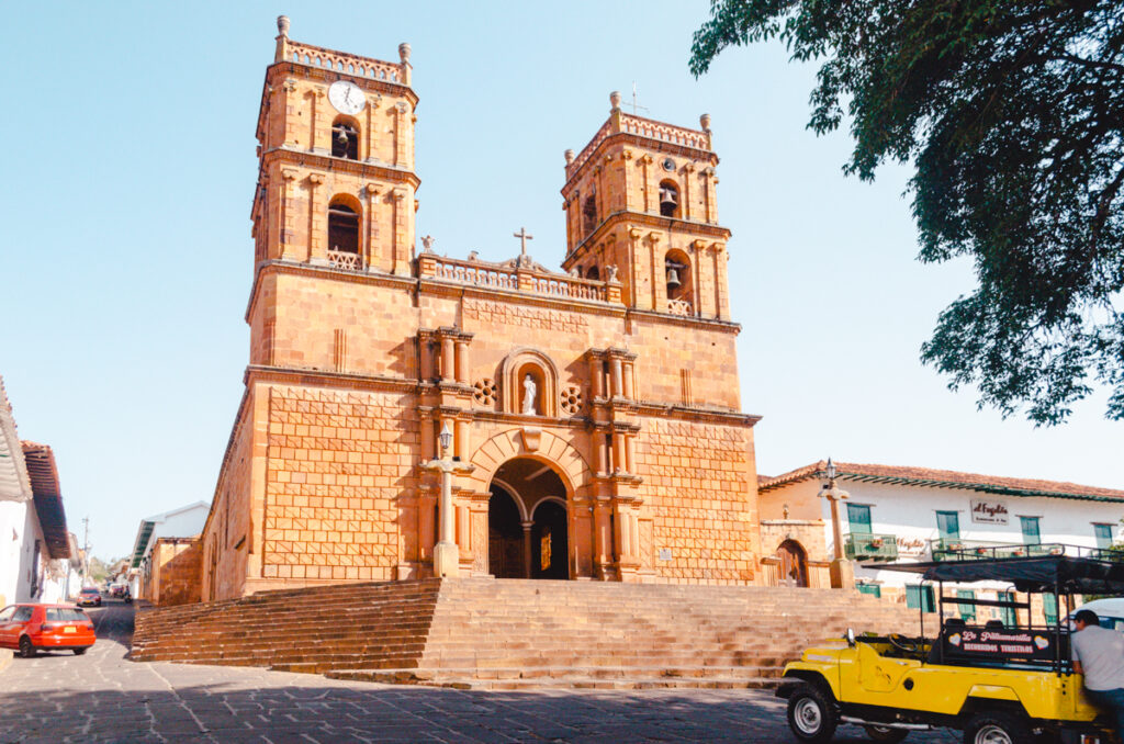 Barichara street scene at the plaza principal with yellow jeep in motion and the church in front him.