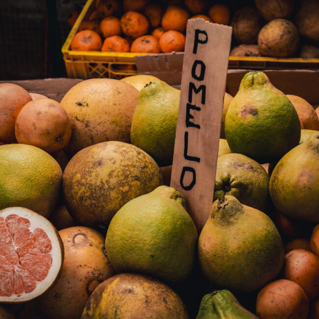 A selection of fresh pomelos lying next to each other at a market. There's a wooden sign sticking out saying 'pomelo'.