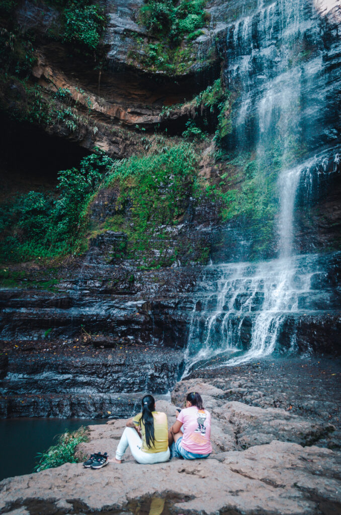 Two individuals sitting on rocks near Juan Curi waterfall, enjoying the serene beauty of nature.