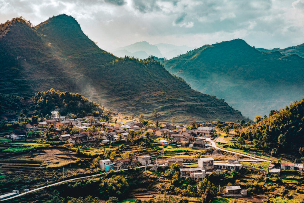 A panoramic view over Ha Giang village. There are mountains in the background with green and golden yellow colors and the sun is giving the town a golden hue.