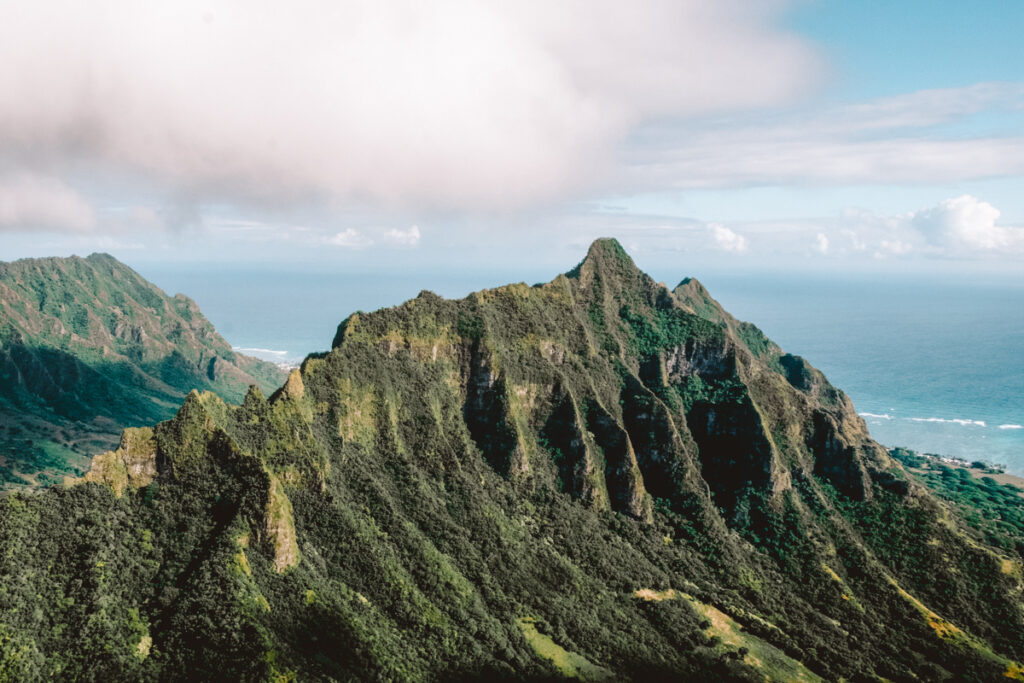 In this photo, you can see a spine-like structure of mountains covered with lush greenery. You can see the ocean in the background.