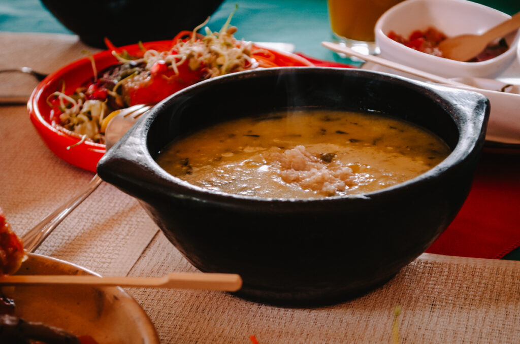 A hot black bown of Colombian soup with quinoa surrounded by other dishes on a table.