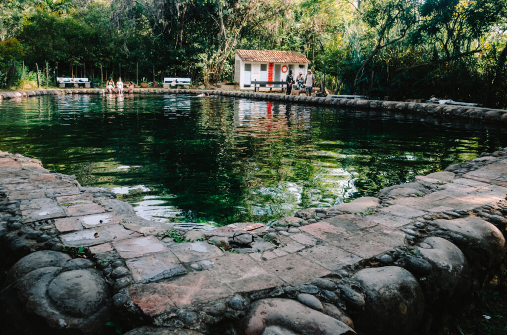 a pond with people in the background surrounded by lush nature in Villa de Leyva