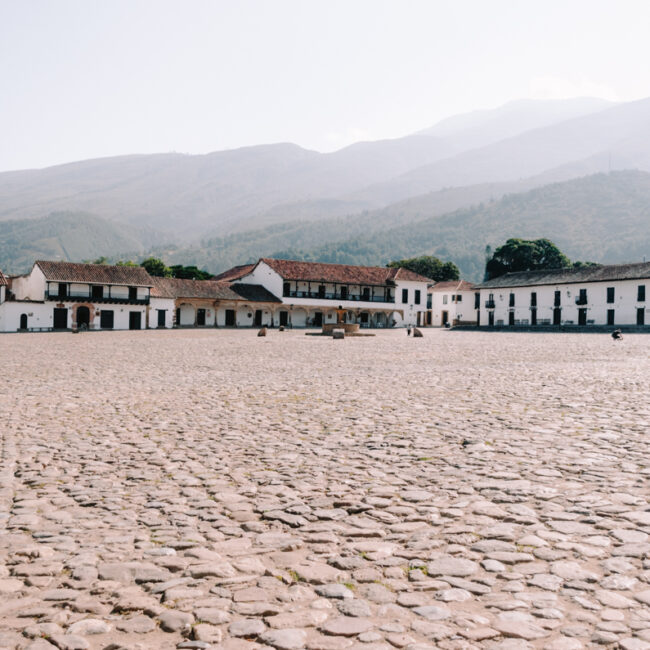 A large stone plaza in Villa de Leyva with buildings and a mountain in the background
