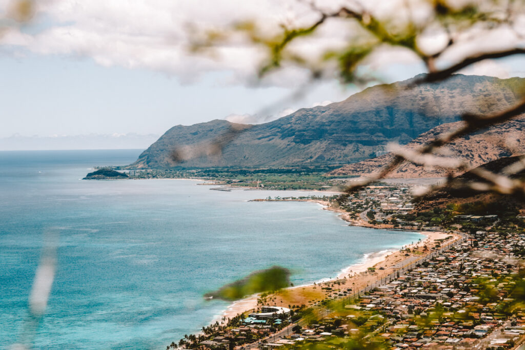 In this photo about Hawaii puns, you can see the beach of Waianae. In the background is a mountain range, the sky is clear and the ocean bright blue.