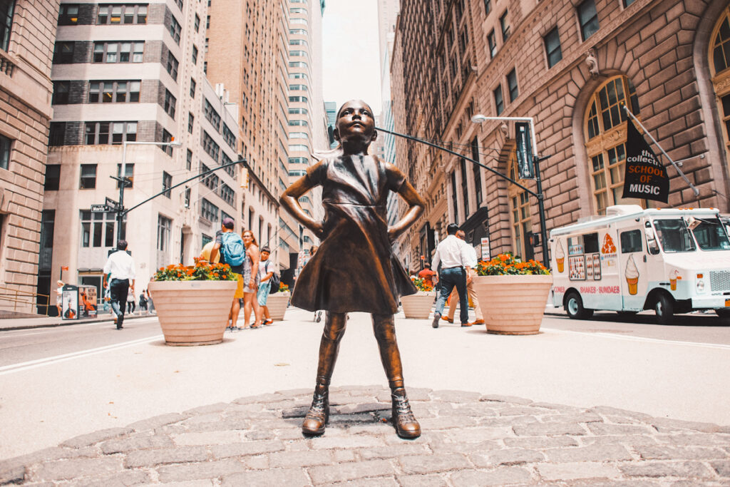 This photo shows a statue of a little girl on Wall street Avenue. She is surrounded by high rise buildings.