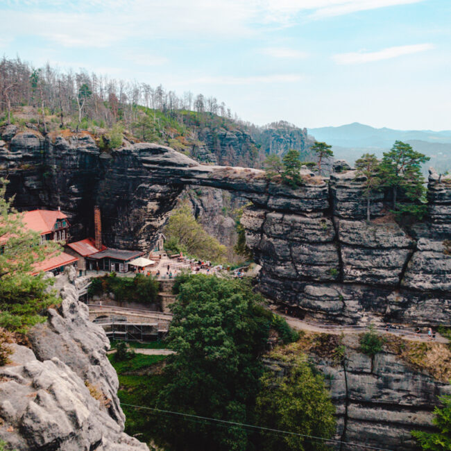 The impressive Pravcicka Brana, a large rock formation, rises dramatically, surrounded by vibrant landscapes and scenic views.