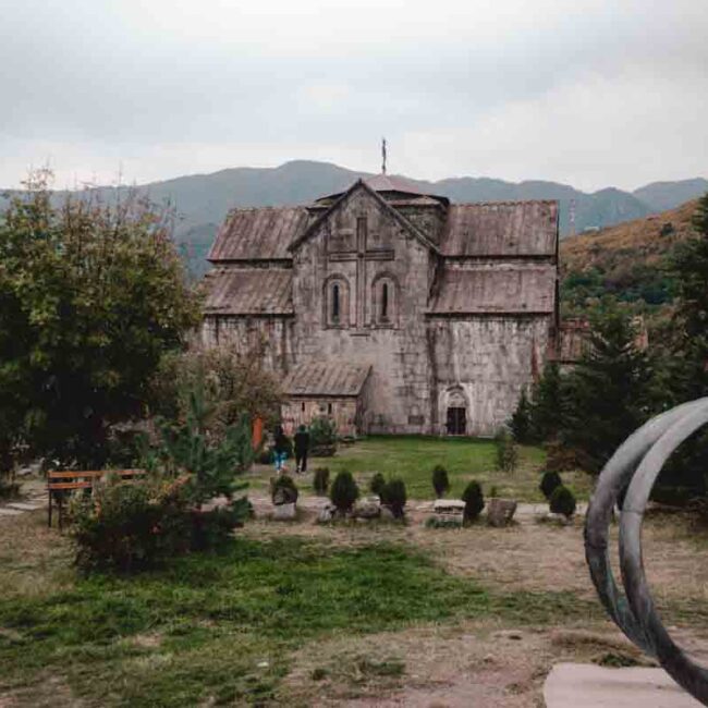 A scenic view of Akhtala Monastery in the mountains, featuring a prominent large metal sculpture in the foreground.